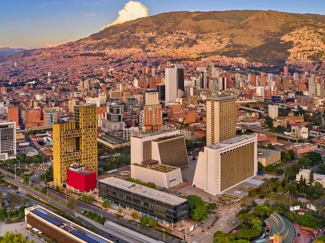 Aerial view of downtown Medellín at sunset, with administrative towers, tree-lined avenues and the Aburrá Valley mountains in the background