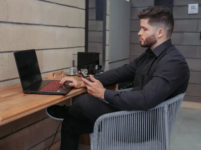Guest in a black shirt working on a laptop and checking his phone at a wooden desk at Living by Armóniko