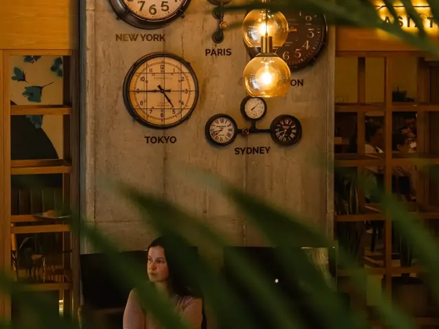 Lobby of Living by Armóniko: a concrete column with clocks showing the time in New York, Paris, Tokyo and Sydney, amber glass pendant lamps and a guest sitting below, seen through palm leaves