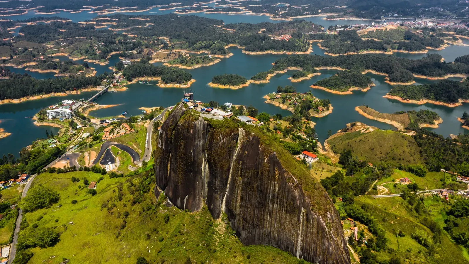 Vista aérea de la Piedra del Peñol, con construcciones en su cima, rodeada por el embalse de Guatapé y sus islas verdes