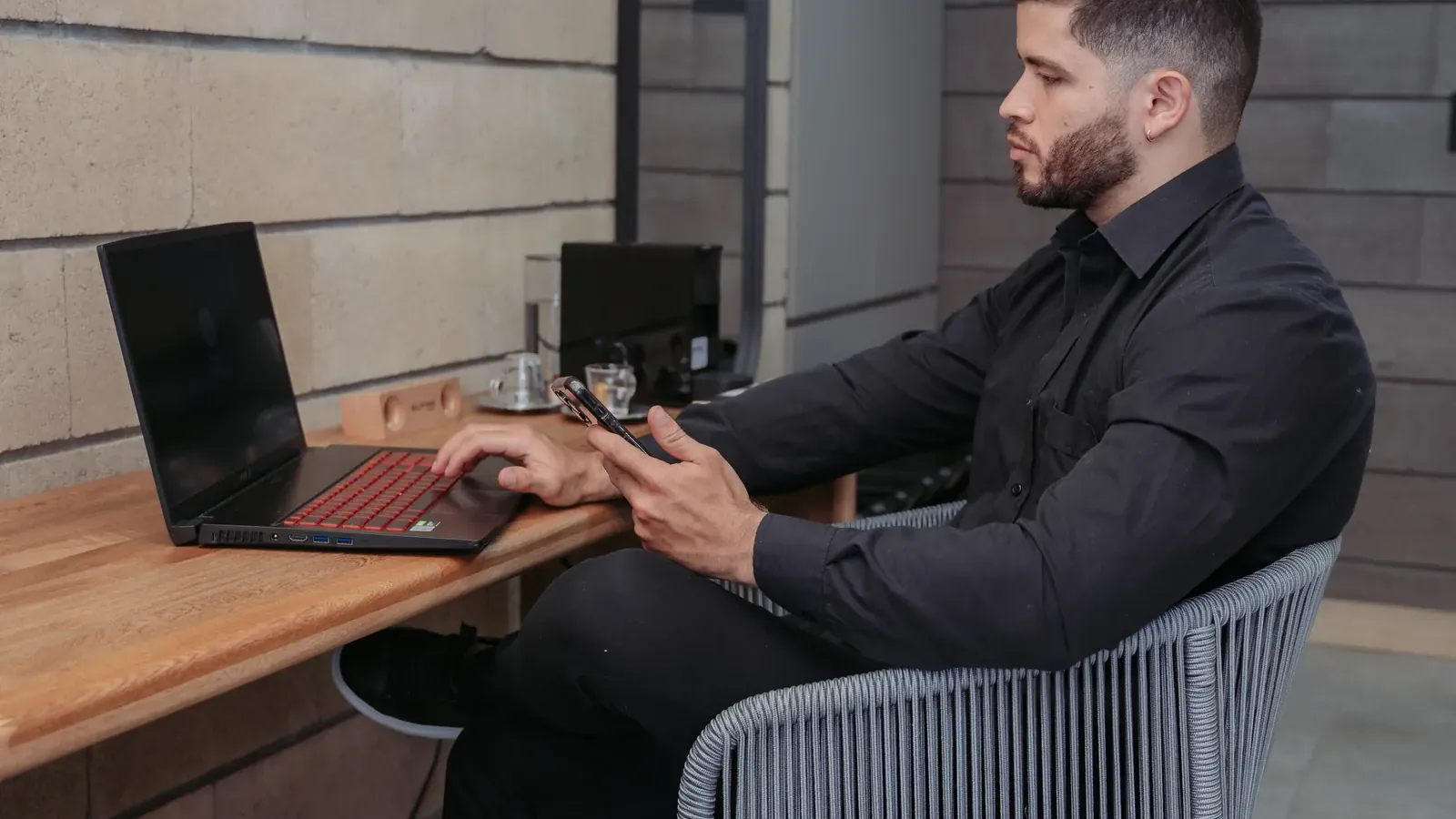 Huésped con camisa negra trabaja en un portátil y revisa su celular en un escritorio de madera de Living by Armóniko