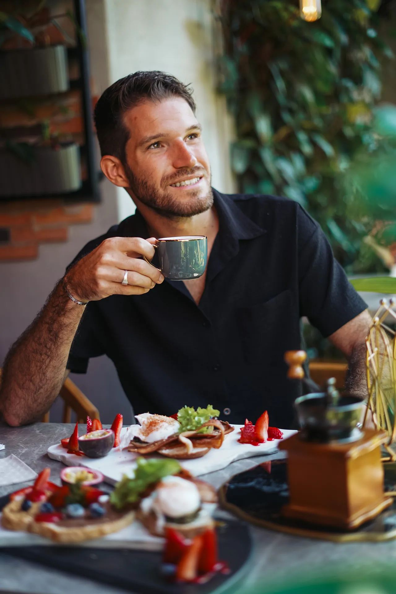 Smiling guest holding a cup of coffee over a breakfast of poached eggs and strawberries at Botswana Café Bar