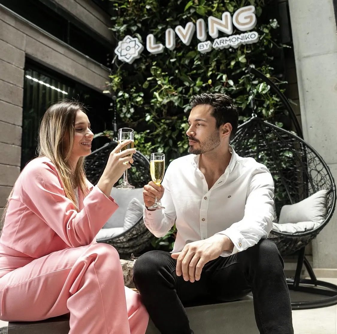 Couple toasting with champagne in front of the vertical garden and the Living by Armóniko sign