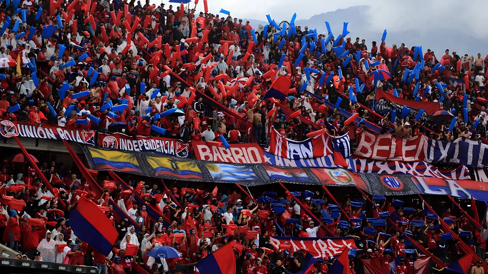 Stadium stand packed with fans waving red and blue flags and banners during a football match in Medellín